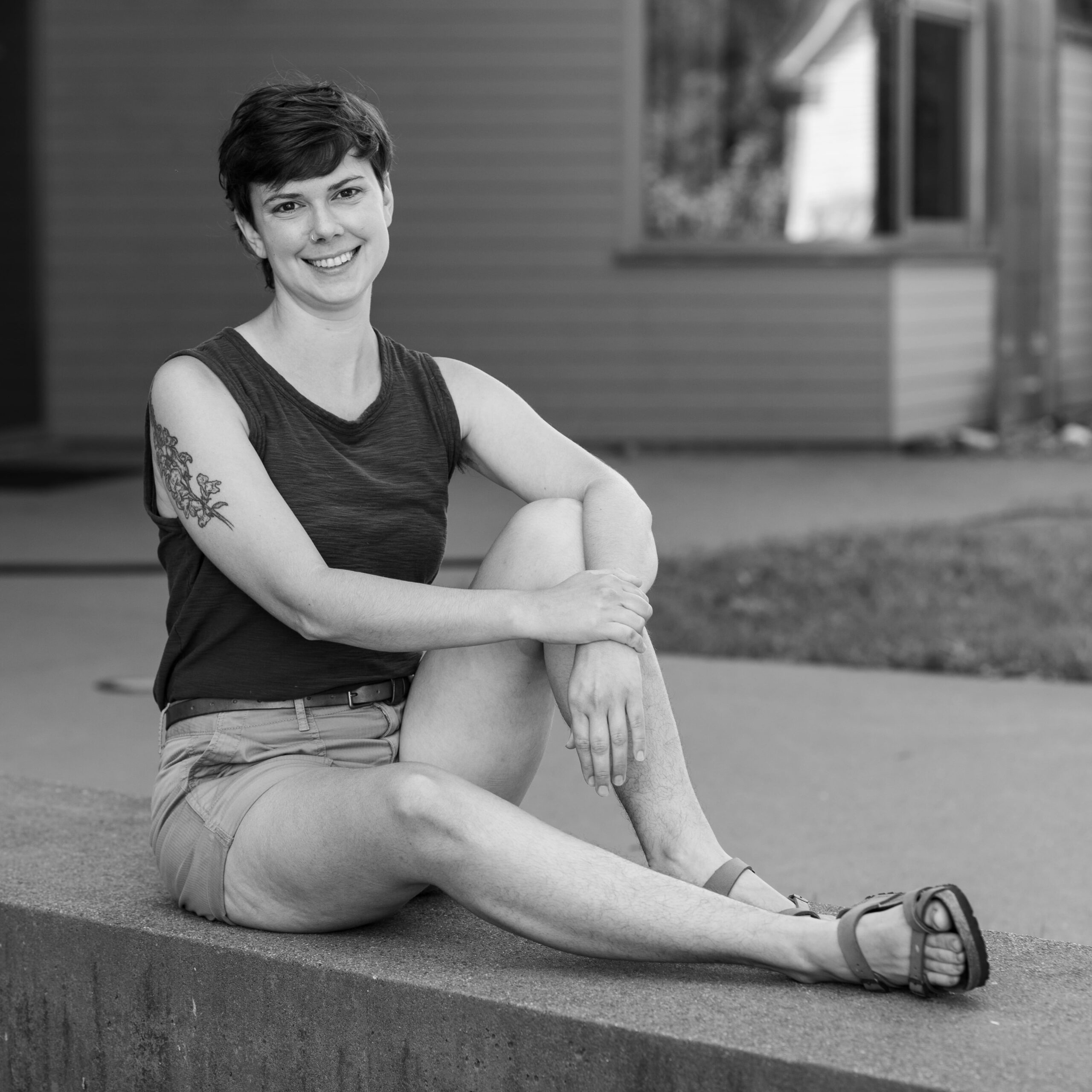 leigh in shorts and tank top, arms crossed over one knee in black and white